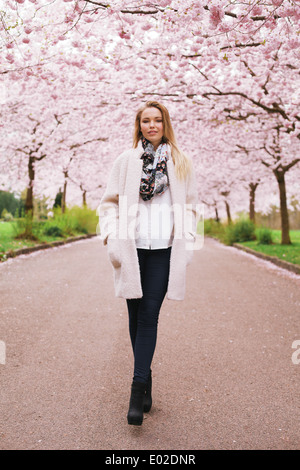 In voller Länge Portrait von stilvolle junge Frau, die im Frühlingspark wandern. Modische weibliches Modell im Frühjahr blühen Park - Natur Stockfoto