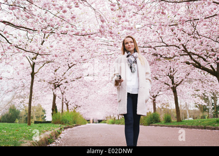 Schöne junge Frau mit Handy anhören von Musik im Frühling blühen Park. Attraktive junge Frau genießen Musik. Stockfoto
