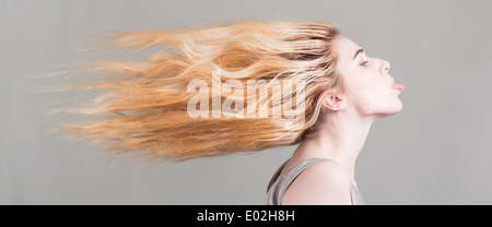 Blonde Frau mit langen Haaren, die fliegen, ihre Zunge heraus. Konzeptbild von Freiheit, starke Haltung und Persönlichkeit. Stockfoto