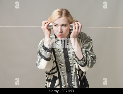 Blonde Frau mit Blechdose Telefon hören. Konzeptbild von Spionage, Überwachung und Kommunikation. Stockfoto