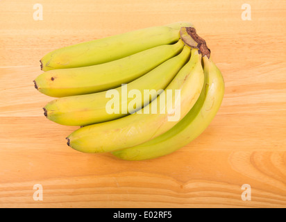 Eine Reihe von grünen Bananen auf einem Holztisch Stockfoto