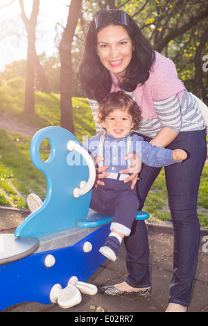 Mutter und Kleinkind Jungen Spaß im Park an der Wippe und stehend im Sonnenstrahl Stockfoto