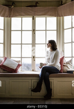 Eine junge Frau sitzt an einem Fensterplatz mit einer Tasse Tee. Stockfoto