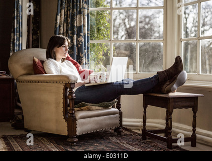 Eine junge Frau mit ihren Füßen mit einem Laptop zu Hause entspannen. Stockfoto