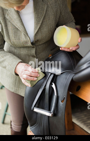 Eine Frau, Reinigung und Vorbereitung Tack und Sattel im Hof des einen Reitstall.