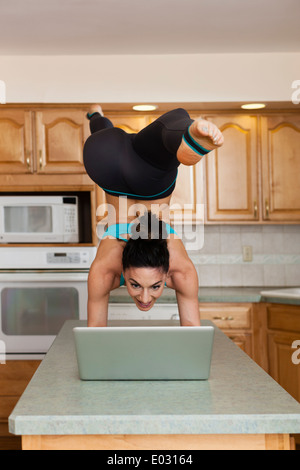 Eine Frau macht einen Handstand balancieren auf einem Küche Top und die Überprüfung ihres Laptops. Stockfoto