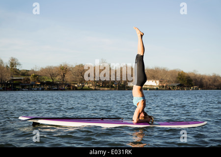 Eine Frau macht einen Kopfstand auf einem Paddle Board auf See Stockfoto