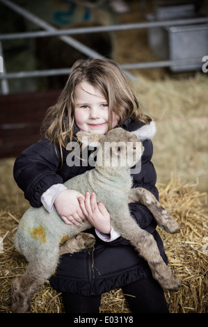 Ein Mädchen hält ein kleines Neugeborenes Lamm. Stockfoto