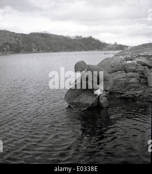 der 1950er Jahre und historische Bild zeigt einen Mann, der junge Lachse in einen See. Stockfoto