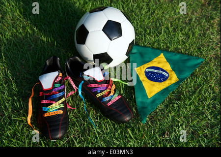 Viel Glück Fußballschuhe Fußball Fußball Stollen geschnürt mit brasilianischen Wunsch Bändern auf grünen Rasen-Fußballplatz mit Brasilien-Flagge Stockfoto