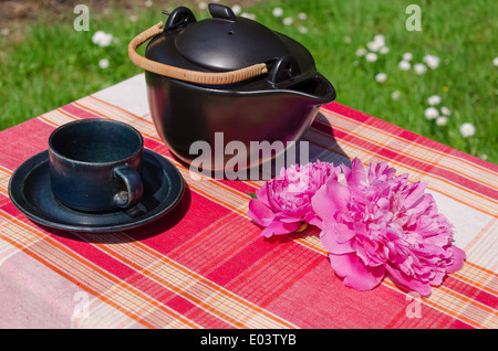 schwarze Keramik Teekanne und Tasse mit Pfingstrose Blüte auf Tisch im freien Stockfoto