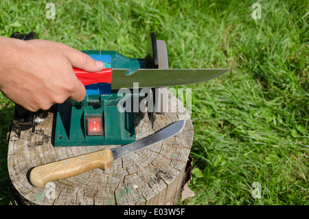 Hand-Schleifer Messer mit Elektrowerkzeug auf Outdoor-Log. Stockfoto