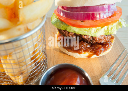 Klassische Burger und Salat mit Beilage Pommes frites oder Chips und Tomatenketchup auf einer Holzplatte Stockfoto