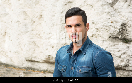 Hübscher junger Mann mit Denim Shirt sitzt im Freien vor Stein Stockfoto