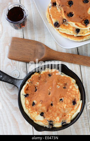 Hohen Winkel Schuss von einer gusseisernen Pfanne mit einem ein frisch zubereitetes Heidelbeer-Pfannkuchen. Eine Platte mit mehr Pfannkuchen Stockfoto