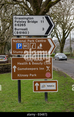 Auto nähert sich 4 verschiedene Verkehr Verkehrszeichen, 1 über den Anderen, Zeigen & Wegbeschreibungen (3 Braun für Touristen) - Yorkshire Dales, England, UK.