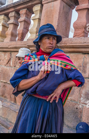 Eine indigene Aymara-Frau, gekleidet in traditioneller Kleidung trägt ihr Baby auf dem Rücken in einem bunten Schal gewickelt. Stockfoto