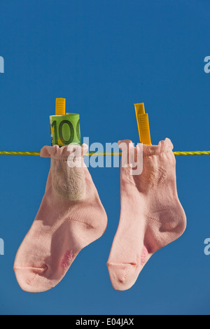 Baby Socken auf der Wäscheleine mit Eurobank Noten. Blauer Himmel., Baby Socken Auf Waescheleine Mit Eurogeldscheinen. Blauer Himmel. Stockfoto