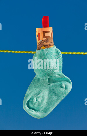Baby Socken auf der Wäscheleine mit Eurobank Noten. Blauer Himmel., Baby Socken Auf Waescheleine Mit Eurogeldscheinen. Blauer Himmel. Stockfoto