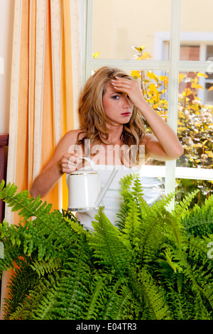 Junge Frau gießt hier Blumen in der Wohnung, Junge Frau Giesst Ihre Blumen in der Wohnung Stockfoto