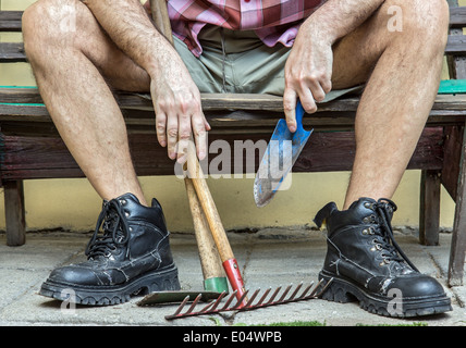 Gärtner mit behaarten Beinen in Stiefel ruhen auf einer Bank Stockfoto