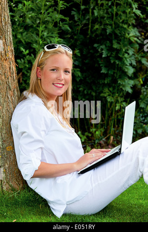 Eine junge Frau mit einem Laptop im Garten sitzt und surft im Internet. WLAN in den Park, Eine Junge Frau Sitzt mit Stockfoto