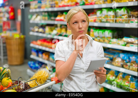 Eine Frau wird zu viel mit der großen Auswahl in einem Supermarkt mit dem Kauf, Eine Frau ist Mit der Großen Auswahl an Ei ebenfalls gefordert. Stockfoto