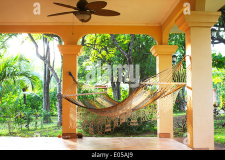 Eine einladende Hängematte hängt eine sonnige Veranda mit den Tropen in den Hintergrund. Stockfoto