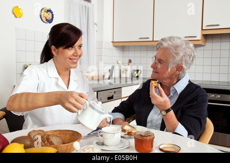 Eine alte Krankenschwester hilft Senior in das Frühstück, Eine Altenpflegerin Hilft Seniorin Beim Fruehstueck Stockfoto