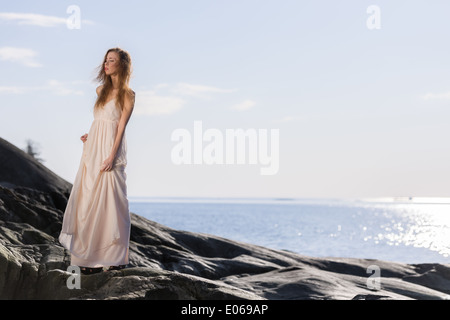 Schöne junge Frau trägt weißes Kleid, skandinavischen Küste und Meer im Hintergrund Stockfoto