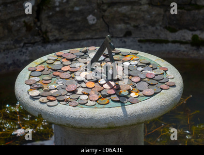 Münzen, die traditionell in wünschen für Glück, hier auf eine Sonnenuhr im Zentrum eines kleinen Teiches in einem formalen Garten Brunnen geworfen Stockfoto