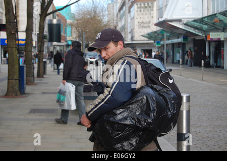 Ein Obdachloser Blicke über die Schulter zeigt seinen Besitz in einen Rucksack und einen schwarzen Müllbeutel enthalten. Stockfoto