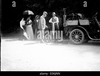 Dieses Foto vom 2. September 1901 zeigt eine Frau mit einem Platten Reifen neben einem Auto aus dem frühen 20. Jahrhundert. Eine Panne auf der Straße ist offensichtlich, da ein Mann assistiert, während ein Sonnenschirm für Schatten benutzt wird. Die Szene wird in Cierp-Gaud aufgenommen, aufgenommen mit historischer Bedeutung. Stockfoto
