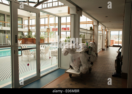 Wagen Sie mit schmutzige Bettwäsche und Reinigung Ausrüstung wartet außerhalb der Zimmer in einem Hotel in Neu-England.     Pool über Glastüren. Stockfoto