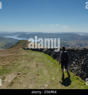 Eine junge Frau zu Fuß entlang einer Steinmauer, absteigend von einem Hügel in Richtung Ambleside an einem sonnigen Frühlingstag. Stockfoto