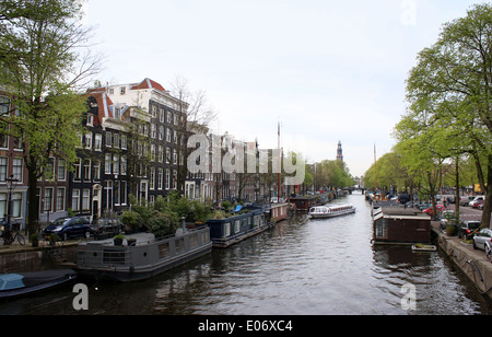 Historische Häuser und alte Boote entlang Prinsengracht Kanal in Amsterdam, Niederlande, Weterkerk Turm in Ferne Stockfoto