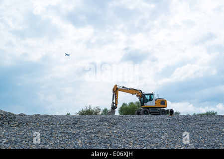 Bild von einem Mobilbagger auf einen Steinbruch Tipp mit zusätzlichen Schaufel und Flugzeug im Hintergrund ab Stockfoto