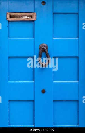 eine blaue Holztür mit einem Türklopfer und einen vollen Briefkasten Stockfoto