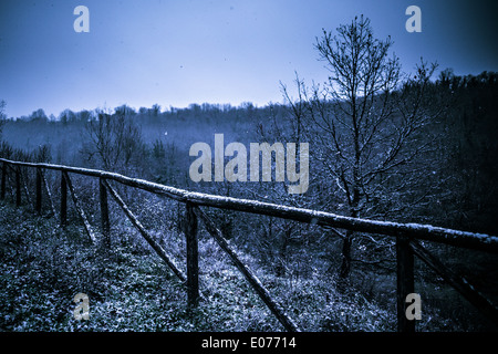 ein Holzzaun mit Schnee bedeckt. im Hintergrund fallen die Schneeflocken in einer finsteren Nacht Stockfoto