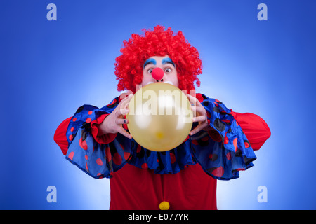 Clown im roten Kostüm mit Ballon in Händen auf blauem Hintergrund Stockfoto