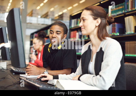 Junge Studenten sitzen am Tisch mit dem Computer für die Forschung. Junge Menschen unter Informationen vom Computer. Stockfoto