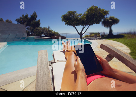 Entspannte Frau mit digital-Tablette am Pool. Gebräunte weibliche Modell Sonnenbaden und Tablet-PC am Pool hält. Stockfoto