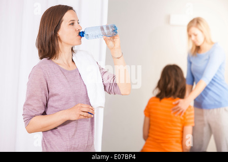 Frau trinkt aus Flasche Wasser, Physiotherapeut und Client im Hintergrund Stockfoto