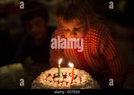 Kleines Mädchen bläst Geburtstagskerzen auf Kuchen Stockfoto