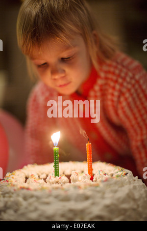 Kleines Mädchen bläst Geburtstagskerzen auf Kuchen Stockfoto