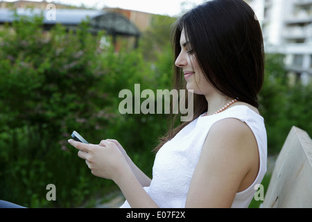 Seite Ansicht Porträt einer Frau auf der Bank im Freien sitzen und am Telefon eingeben Stockfoto