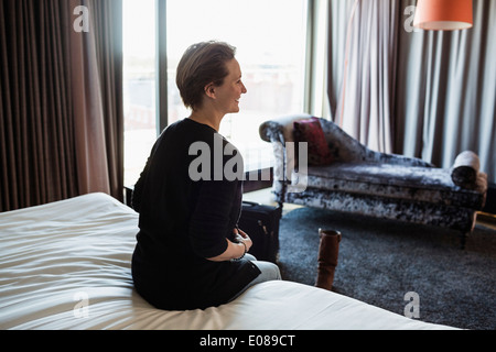 Rückansicht des lächelnden Geschäftsfrau sitzt auf dem Bett im Hotelzimmer Stockfoto