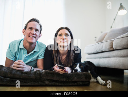 Paar mit Hund vor dem Fernseher liegend am Boden zu Hause Stockfoto