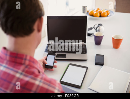 Erhöhte Ansicht des Mannes mit Smartphone mit digitalen Tablet und Laptop auf Tisch Stockfoto