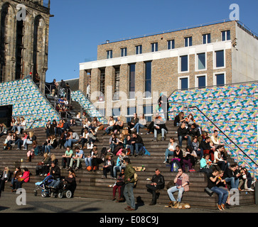 Menschen genießen die Frühlingssonne auf der Treppe des Fremdenverkehrsamtes auf dem Hintergrund der neuen Schüler-Gesellschaft in Groningen Stockfoto